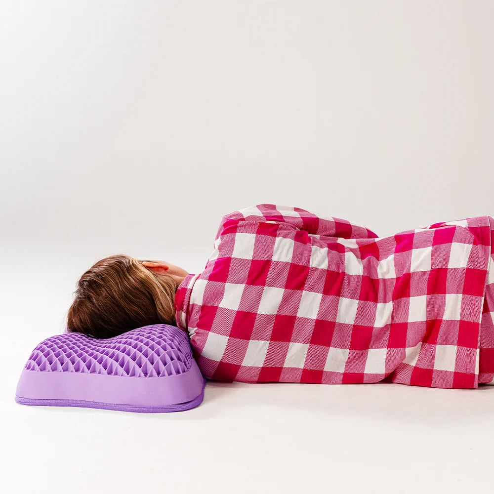 Mulher deitada de lado no travesseiro airgelly 100% lavável da iws na cor roxa e formato ergonômico com as costas virada para a tela destacando a correção de postura que ocorre quando usamos um travesseiro ideal como o airgelly iws ergonômico