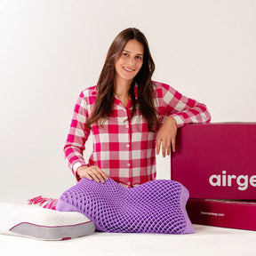 Mulher sorridente de cabelo castanho e pele claro sentada no chão com seu airgelly roxo em formato borboleta no colo, com outro airgelly com capa de bamboo ao seu lado enquanto apoia o braço na embalagem do airgelly iws 100% lavável 